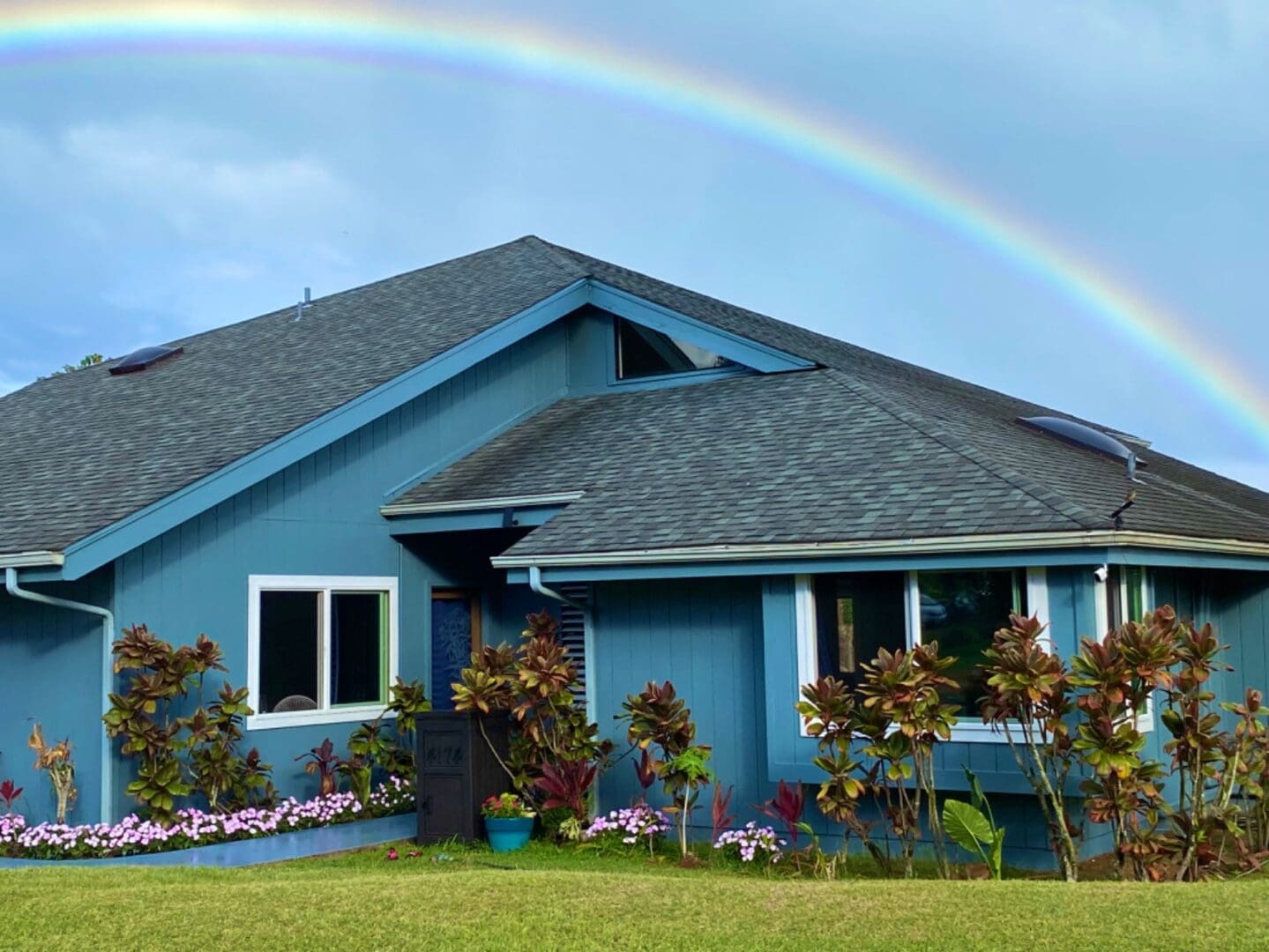 A rainbow over the house in front of some flowers.