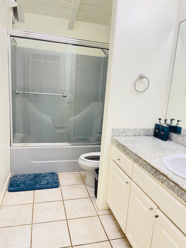 A bathroom with white tile and blue rug.