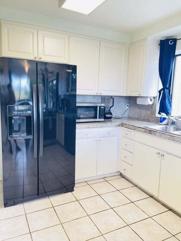 A kitchen with white cabinets and black refrigerator.