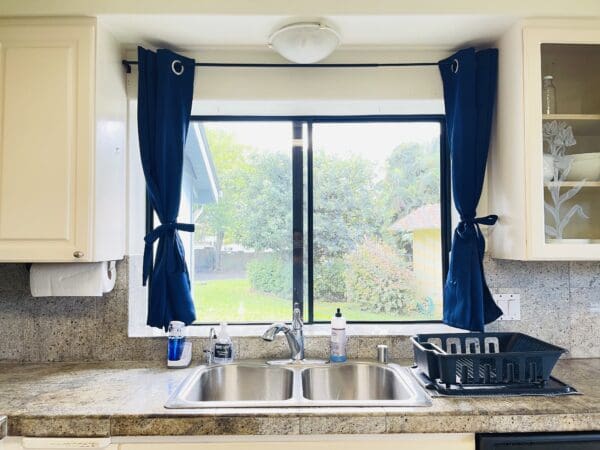 A kitchen sink with blue curtains on the window.