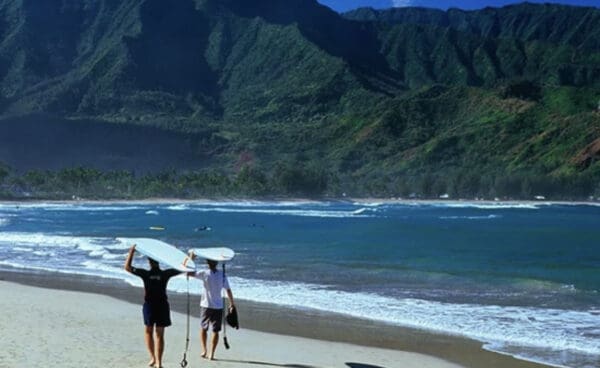 Two people walking on the beach with surfboards.