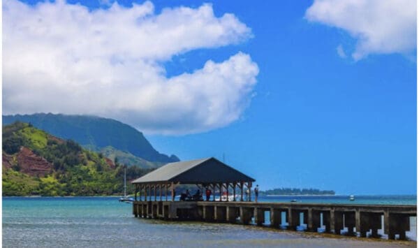 A dock with people sitting on it and mountains in the background.