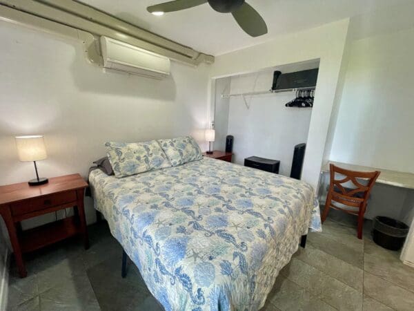 A bedroom with a bed, desk and fan.