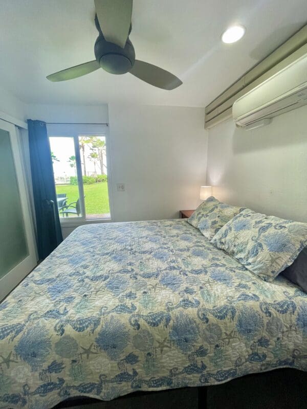 A bedroom with a bed, ceiling fan and sliding glass doors.