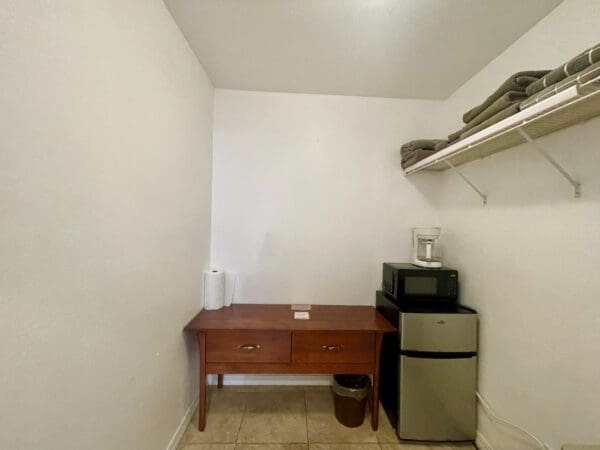 A room with a desk, microwave and refrigerator.