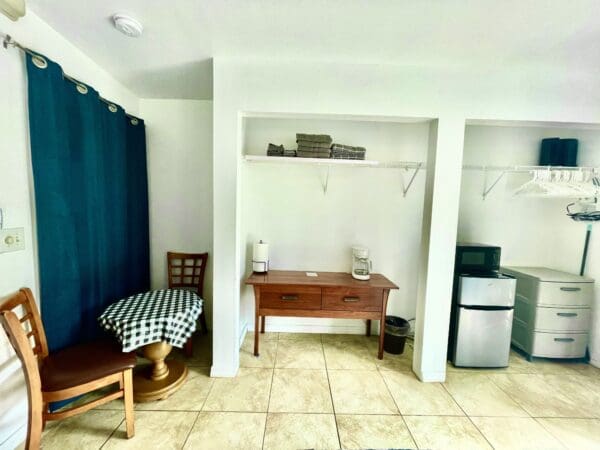 A room with a table, chair and refrigerator.