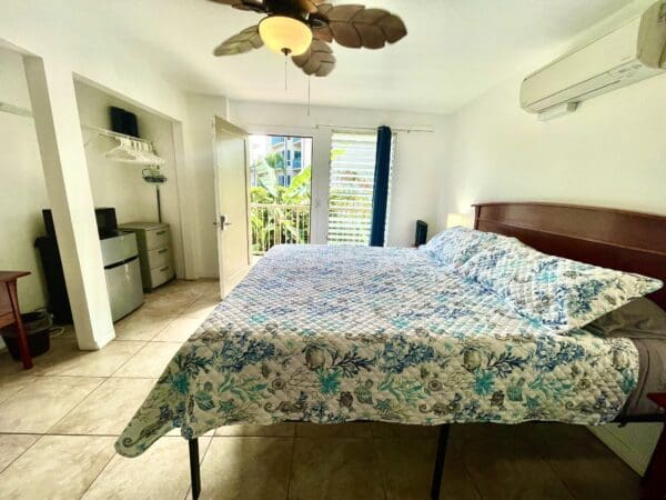 A bedroom with a bed, fan and balcony.