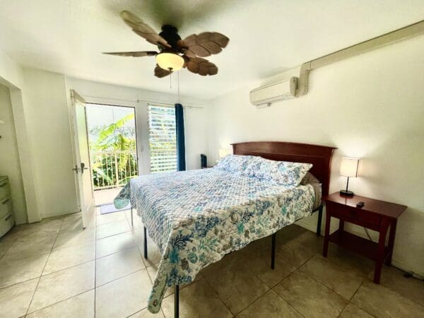 A bedroom with a bed, ceiling fan and balcony.