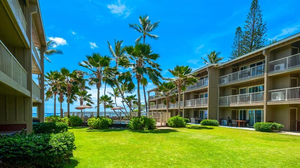 A hotel with palm trees and lawn in front of it.