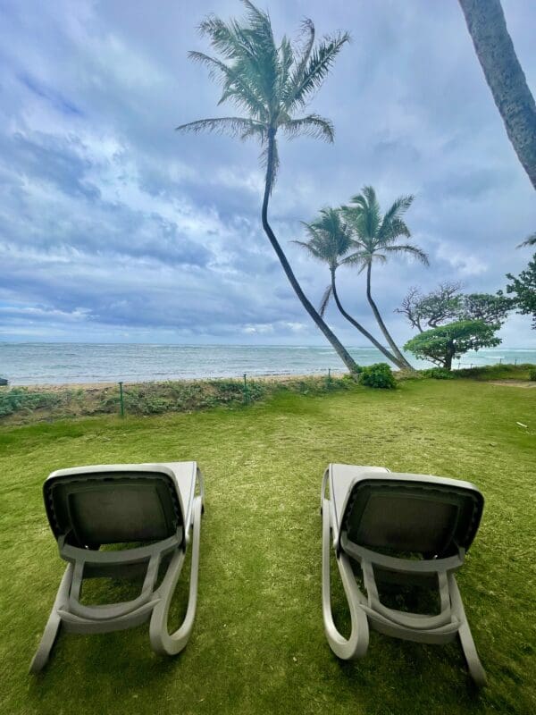 Two lawn chairs in the grass near a beach.